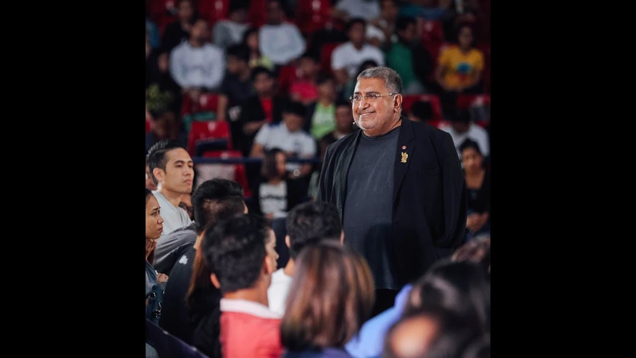 Dr Mel Gill standing among a seated event audience